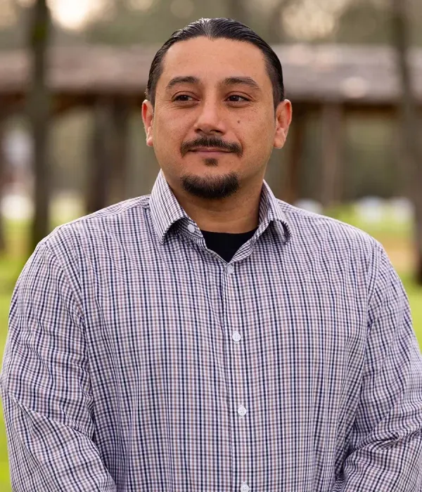 Daniel Burnett standing outdoors wearing a checkered shirt with a calm expression.