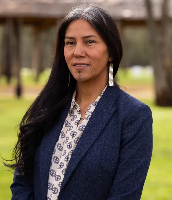 Malissa Tayaba standing outdoors in a blue blazer, wearing traditional earrings and displaying chin markings.